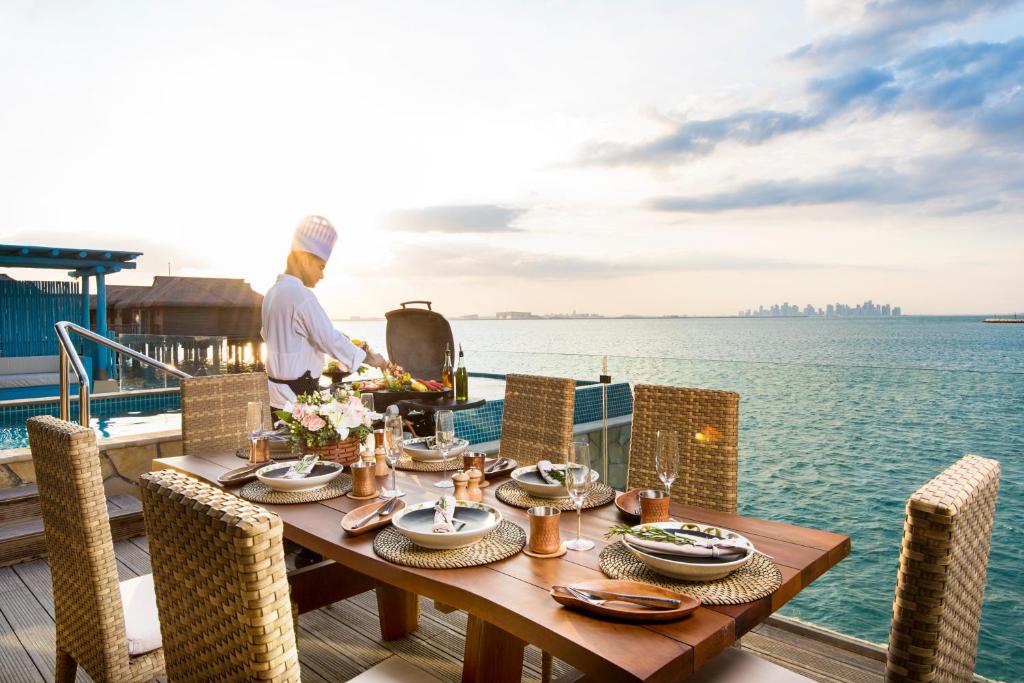 A table set on a deck over the sea, with a chef at the grill and the Doha skyline beyond
